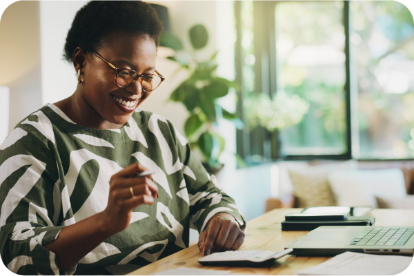 Woman looking a her computer with a calculator in front of her smiling